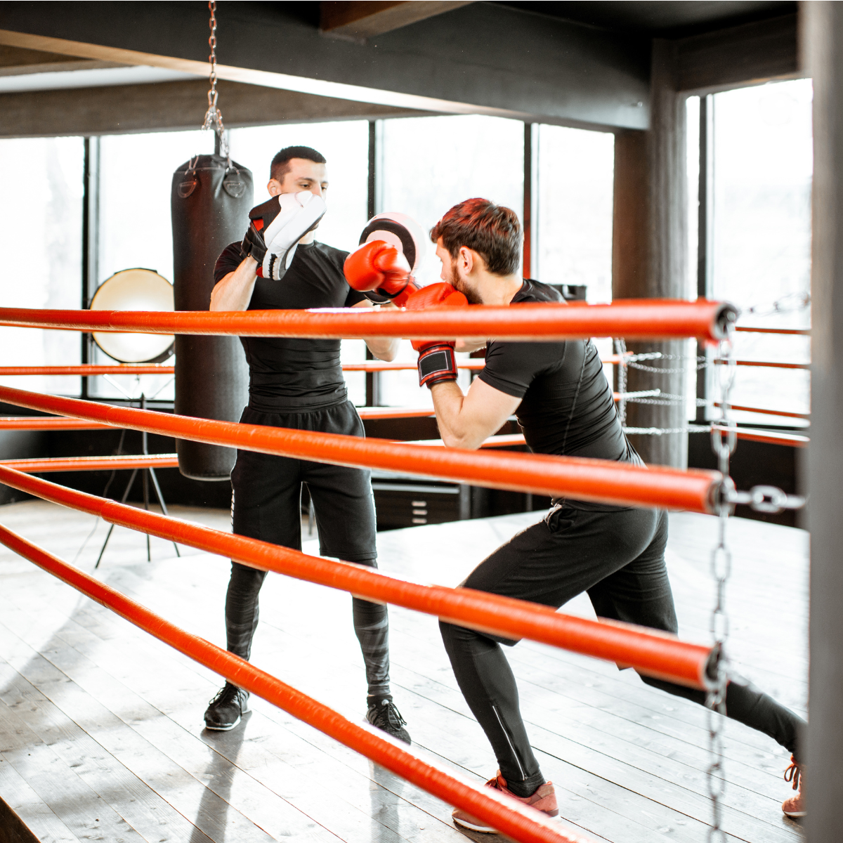A Sentry Jiu-Jitsu boxing coach holding focus mitts as a member throws a punch inside the ring